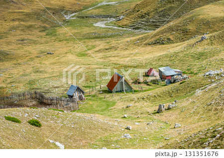 Distant view of a small house with a shed on a lonely hill surrounded by mountain ridges, natural rural scenery Distant view of a small house with a shed on a lonely hill surrounded by mountain ridges, natural rural scenery 131351676