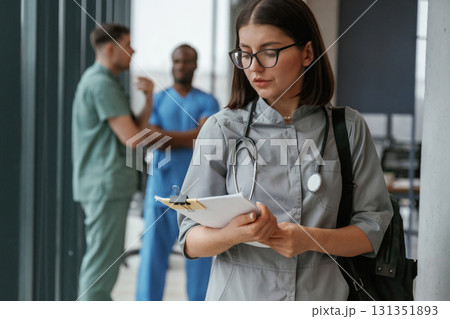 Beautiful woman in glasses is standing. Group of doctors are together indoors 131351893