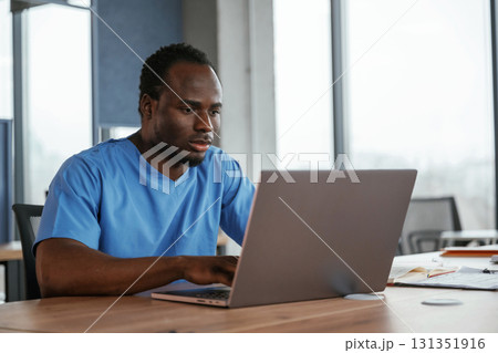 Doctor is sitting by the table with laptop in clinic 131351916