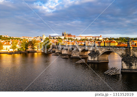 Early morning light casts a glow on Prague Castle and Charles Bridge, reflecting beauty over the Vltava River. The old town awakens as clouds drift above the historic skyline. Early morning light casts a glow on Prague Castle and Charles Bridge, reflecting beauty over the Vltava River. The old town awakens as clouds drift above the historic skyline. 131352019