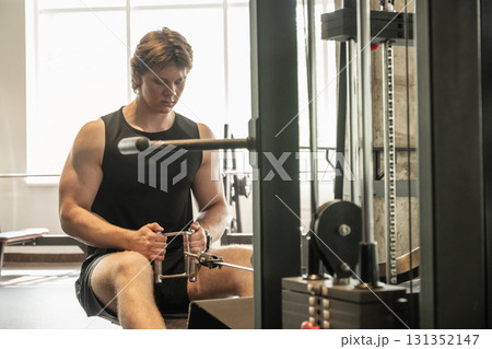 Bodybuilder and sporty man exercising on low rowing machine at gym. Muscular build. Healthy lifestyle Bodybuilder and sporty man exercising on low rowing machine at gym. Muscular build. Healthy lifestyle 131352147