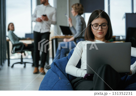 Smart woman is sitting and uses laptop. People are working in the office with bean bags chairs in it 131352231