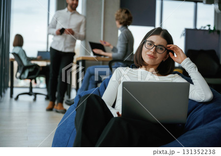Smart woman is sitting and uses laptop. People are working in the office with bean bags chairs in it Smart woman is sitting and uses laptop. People are working in the office with bean bags chairs in it 131352238