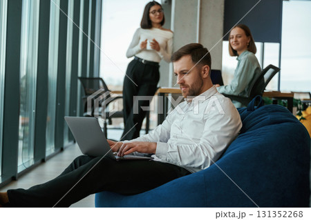 Handsome man is sitting with laptop. People are working in the office with bean bags chairs in it 131352268