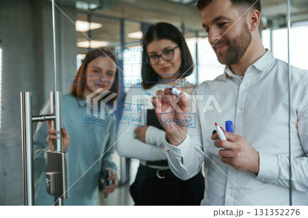 Blue color text. Office workers are creating plan, standing by glass and writing on it Blue color text. Office workers are creating plan, standing by glass and writing on it 131352276