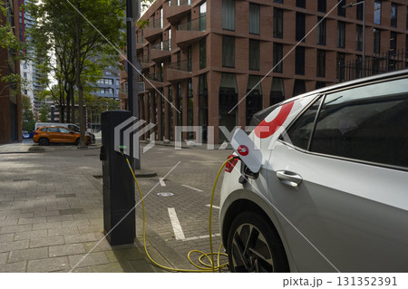 A white electric vehicle charging at a public charging station on a city street. A white electric vehicle charging at a public charging station on a city street. 131352391