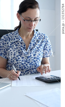 Businesswoman using calculator and filling tax form, calculating expenses and managing financial data in office. Audit and taxes in business Businesswoman using calculator and filling tax form, calculating expenses and managing financial data in office. Audit and taxes in business 131352764