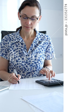 Businesswoman using calculator and filling tax form, calculating expenses and managing financial data in office. Audit and taxes in business 131352774