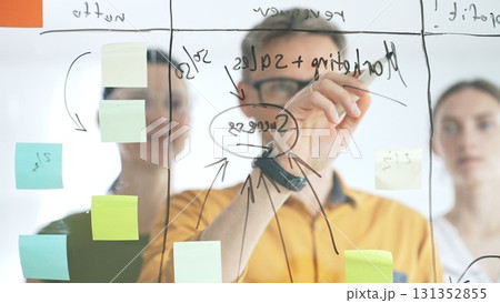 Marketing team collaborating, strategizing business growth with colorful sticky notes on transparent board, targeting revenue and profitability goals Marketing team collaborating, strategizing business growth with colorful sticky notes on transparent board, targeting revenue and profitability goals 131352855