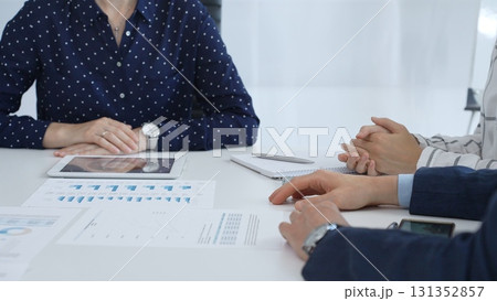 Business people examining and discussing financial documents, studying performance charts on paper and digital tablet during collaborative meeting in modern office 131352857