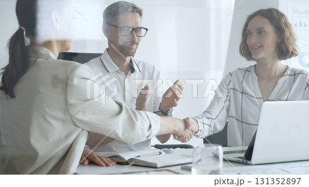 Businesswomen shaking hands after successful negotiation, colleagues clapping, celebrating agreement or partnership in modern office, laptop and documents on table 131352897