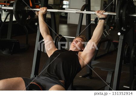 Sporty caucasian man or bodybuilder exercising bench press at fitness center. Male athlete lifting weights. 131352914