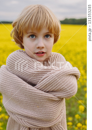 Smiling girl in oversized beige sweater hugging herself in yellow flower field 131353285