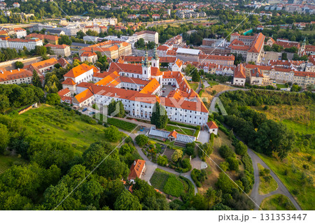 Aerial view of Strahov Monastery bathed in warm sunrise light, surrounded by lush greenery and the cityscape of Prague during the early morning hours. A stunning sight showcasing architectural beauty. 131353447