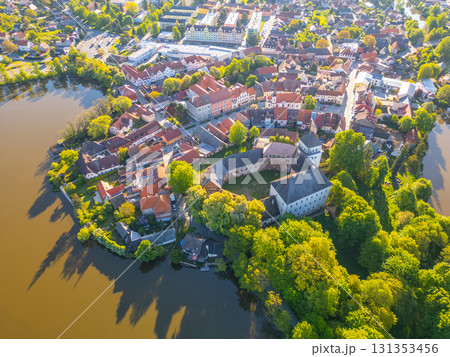 Nestled in lush greenery, Rozmital pod Tremsinem boasts charming houses and a historic castle, highlighting Czechia's rich cultural heritage by a serene water backdrop. 131353456