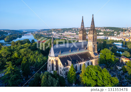 Golden sunlight bathes the Basilica of St. Peter and St. Paul in Prague during a tranquil morning. Surrounded by lush greenery, the historic structure stands majestically against the skyline. 131353478
