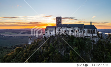 Bezdez Castle, a medieval ruin perched on a hill, offers a stunning aerial view as the sun sets in the evening sky. The silhouette of the tower contrasts beautifully against vibrant colors of dusk. Bezdez Castle, a medieval ruin perched on a hill, offers a stunning aerial view as the sun sets in the evening sky. The silhouette of the tower contrasts beautifully against vibrant colors of dusk. 131353486