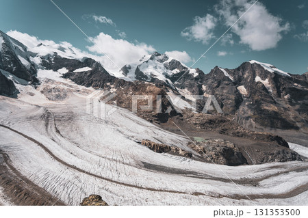 Piz Bernina rises prominently in the Swiss Alps, surrounded by glistening glaciers and dramatic mountain peaks. This stunning landscape showcases nature's grandeur in Graubunden, Switzerland. 131353500