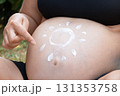 Expecting woman applies sunscreen in the shape of a sun on her bare belly, symbolizing pregnancy care, skin protection, and maternal love under summer sunlight 131353758