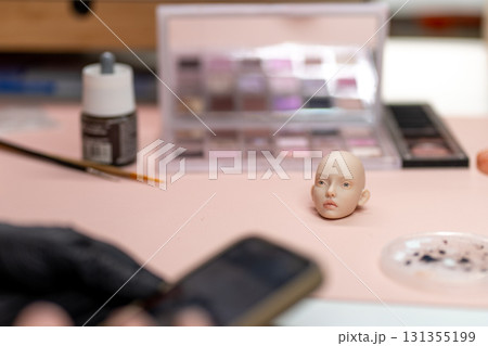 Doll head on table with tools like makeup palette 131355199