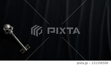 A detailed silver skeleton key with a skull-shaped handle rests diagonally on a dark black draped fabric background, offering ample dramatic copy space. 131356500