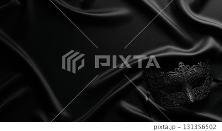 A single ornate black masquerade mask rests elegantly on dark luxurious satin fabric with soft folds and shimmering reflections, offering ample copy space. 131356502