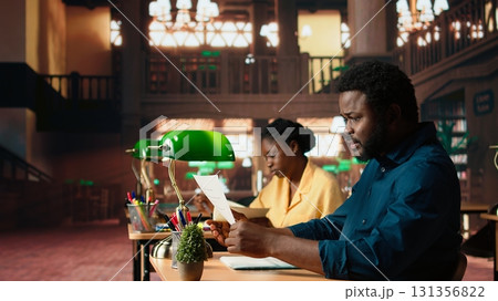 African american college student struggling to study theoretical notes from the last class lesson, learning to prepare for the exam. Anxious frustrated teenager at the campus library. Camera A. 131356822