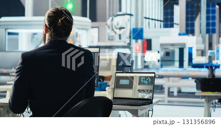 Photovoltaics factory engineer using software on laptop to improve solar panels efficiency. Solar panels manufacturing plant employee researching sustainable solar solutions using notebook, camera B Photovoltaics factory engineer using software on laptop to improve solar panels efficiency. Solar panels manufacturing plant employee researching sustainable solar solutions using notebook, camera B 131356896