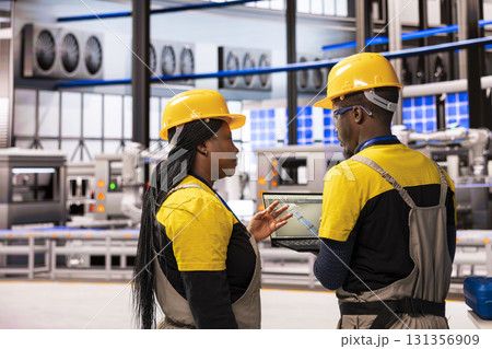 Automated factory engineers tracking production line performance with industrial software on laptop. The smart manufacturing plant features robotic systems and autonomous conveyor belts for precision. 131356909