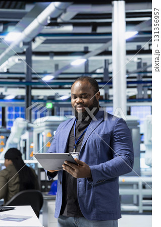 Professional black manager oversees solar panel production line in a facility, ensuring quality manufacturing processes meet corporate goals and green energy standards. Sustainability. 131356957