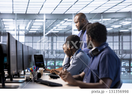 Team of data center office system administrators using programming languages to construct algorithms and build applications. African american server farm IT professionals debugging and optimizing code Team of data center office system administrators using programming languages to construct algorithms and build applications. African american server farm IT professionals debugging and optimizing code 131356998