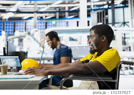 Photovoltaics factory engineer with physical impairment using PC to monitor performance of solar panels manufacturing. Male employee works in disability friendly industrial facility. 131357027