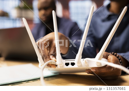 African american woman rebooting their WI FI router modem by moving cables, hoping to solve their ongoing internet issues and speed. Stable wireless connection for freelance tasks. Close up. 131357081