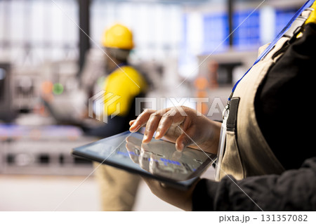 Automation expert with digital device, evaluates system reliability in industrial facility. Black engineer using tablet to troubleshoot smart factory inefficiencies and optimize machinery performance. Automation expert with digital device, evaluates system reliability in industrial facility. Black engineer using tablet to troubleshoot smart factory inefficiencies and optimize machinery performance. 131357082