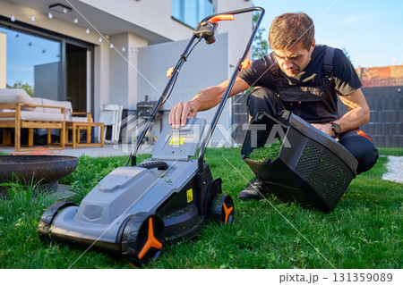 Man cleaning grass container of electric lawn mower 131359089
