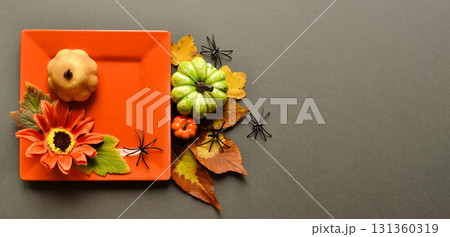 An orange square plate with a sunflower and pumpkin on a gray background with pumpkins, leaves, and spiders. Autumn composition. An orange square plate with a sunflower and pumpkin on a gray background with pumpkins, leaves, and spiders. Autumn composition. 131360319
