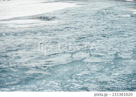 A serene river flows through a snowy landscape, surrounded by mountains. The water is clear and reflects the winter scenery, evoking a sense of calm and mindfulness. 131361020