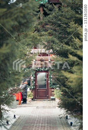 A cozy wooden cabin decorated for Christmas, surrounded by evergreen trees. Snow covers the ground, creating a winter vacation atmosphere. 131361080