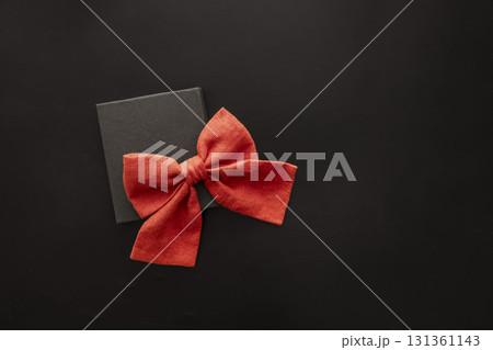 A black gift box with a large red bow on a dark background. The scene conveys a festive atmosphere suitable for Black Friday sales. A black gift box with a large red bow on a dark background. The scene conveys a festive atmosphere suitable for Black Friday sales. 131361143