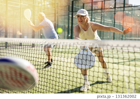 Determined sporty older woman doing her best playing padel in court 131362002