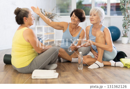 Mature women talking to each other sitting on the floor in fitness studio 131362126