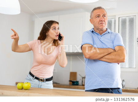 Adult daughter, talking on a mobile phone, is trying to prove her case to a frustrated father Adult daughter, talking on a mobile phone, is trying to prove her case to a frustrated father 131362576