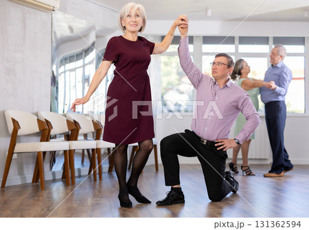 Happy couple enjoying retro ballroom dancing in dance salon, man standing on knee and holding hand of woman 131362594