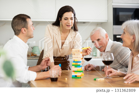 Joyful senior parents and young couple sitting around table playing brick game Joyful senior parents and young couple sitting around table playing brick game 131362809
