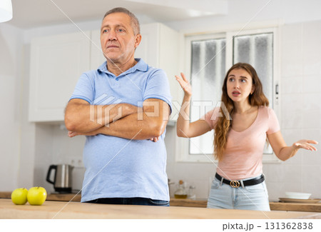Adult daughter scolds an elderly father while he is preparing dinner in kitchen Adult daughter scolds an elderly father while he is preparing dinner in kitchen 131362838