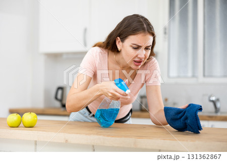Displeased housewife cleaning dinning table with rag in kitchen 131362867