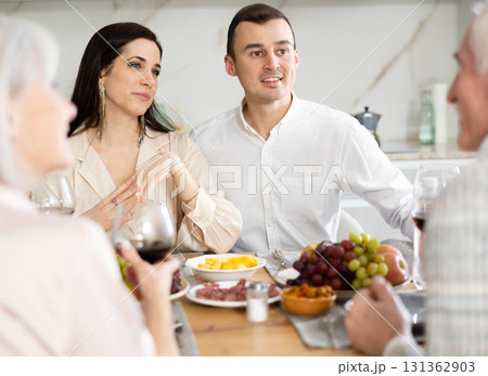 Cheerful young couple chatting with elderly parents at dinner table 131362903
