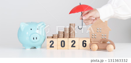Happy New Year 2026 with red umbrella over money stack. Insurance, real estate, Home, car, loan, tax, investment, mortgage, financial, savings, protection and safety 131363332
