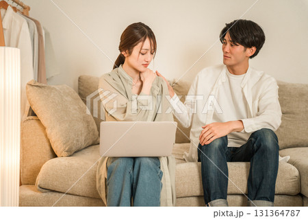 リビングのソファでパソコンで仕事をする妻を心配そうに見つめる夫(残業,持ち帰り残業,隠れ残業) リビングのソファでパソコンで仕事をする妻を心配そうに見つめる夫(残業,持ち帰り残業,隠れ残業) 131364787