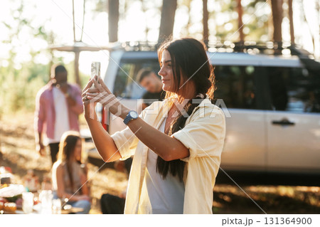 Woman is using smartphone, capturing a photo. Group of friends are having fun together in the forest 131364900